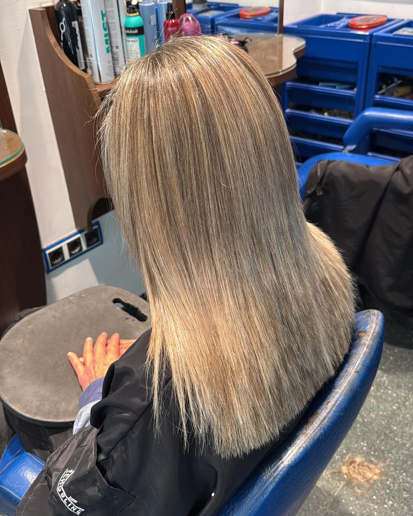 Cabello largo y liso con mechas rubias y cenizas, visto desde atrás en una peluquería.