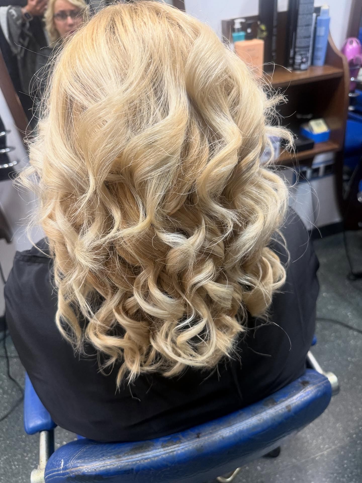 Cabello rubio con rizos definidos y ondas suaves visto desde atrás en un salón profesional.